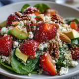 Refreshing quinoa salad featuring ripe strawberries, diced avocado, and fresh spinach, drizzled with zesty lemon-honey dressing.