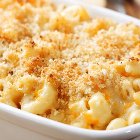 Spoon serving creamy cheddar macaroni and cheese onto a rustic wooden table.
