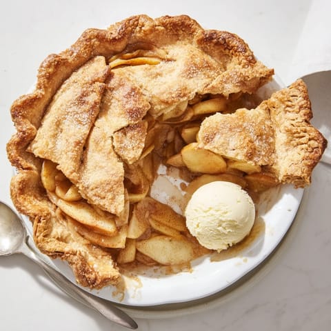 Apple Pie cools on a wire rack, its sugary filling bubbling through lattice vents, ready to be served with vanilla ice cream.