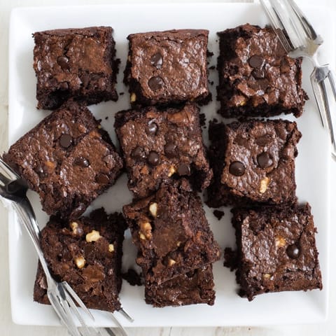 Warm, freshly baked brownies arranged in squares on parchment, perfect for sharing with vanilla ice cream.