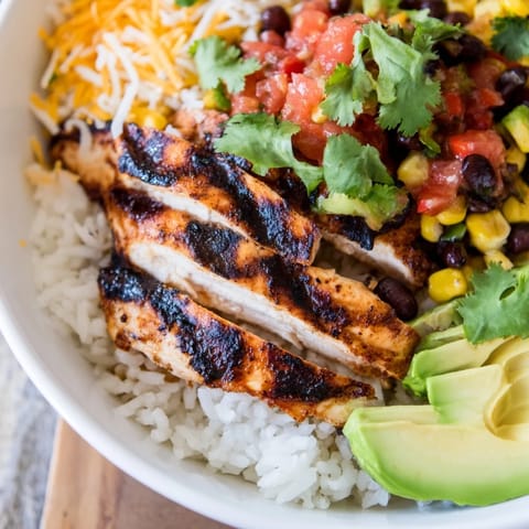A finished Spicy Chicken Burrito Bowl topped with cheese, cilantro, and lime wedges, ready to enjoy.