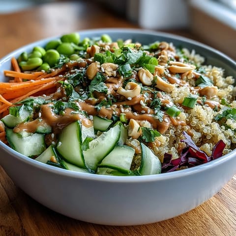 A vibrant Thai Coconut Quinoa Bowl topped with crisp veggies, drizzled with creamy peanut sauce and sesame seeds.