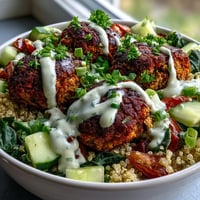 Crisp baked falafel and fluffy quinoa form the base of this vibrant Falafel Quinoa Salad Bowl, topped with diced cucumber and halved cherry tomatoes. A drizzle of creamy garlic tahini sauce adds a rich finish to this wholesome vegetarian main dish.