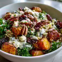 Harvest Kale Quinoa Bowl with roasted sweet potatoes, kale, pecans, cranberries, blue cheese, and lemon tahini dressing in a rustic bowl.